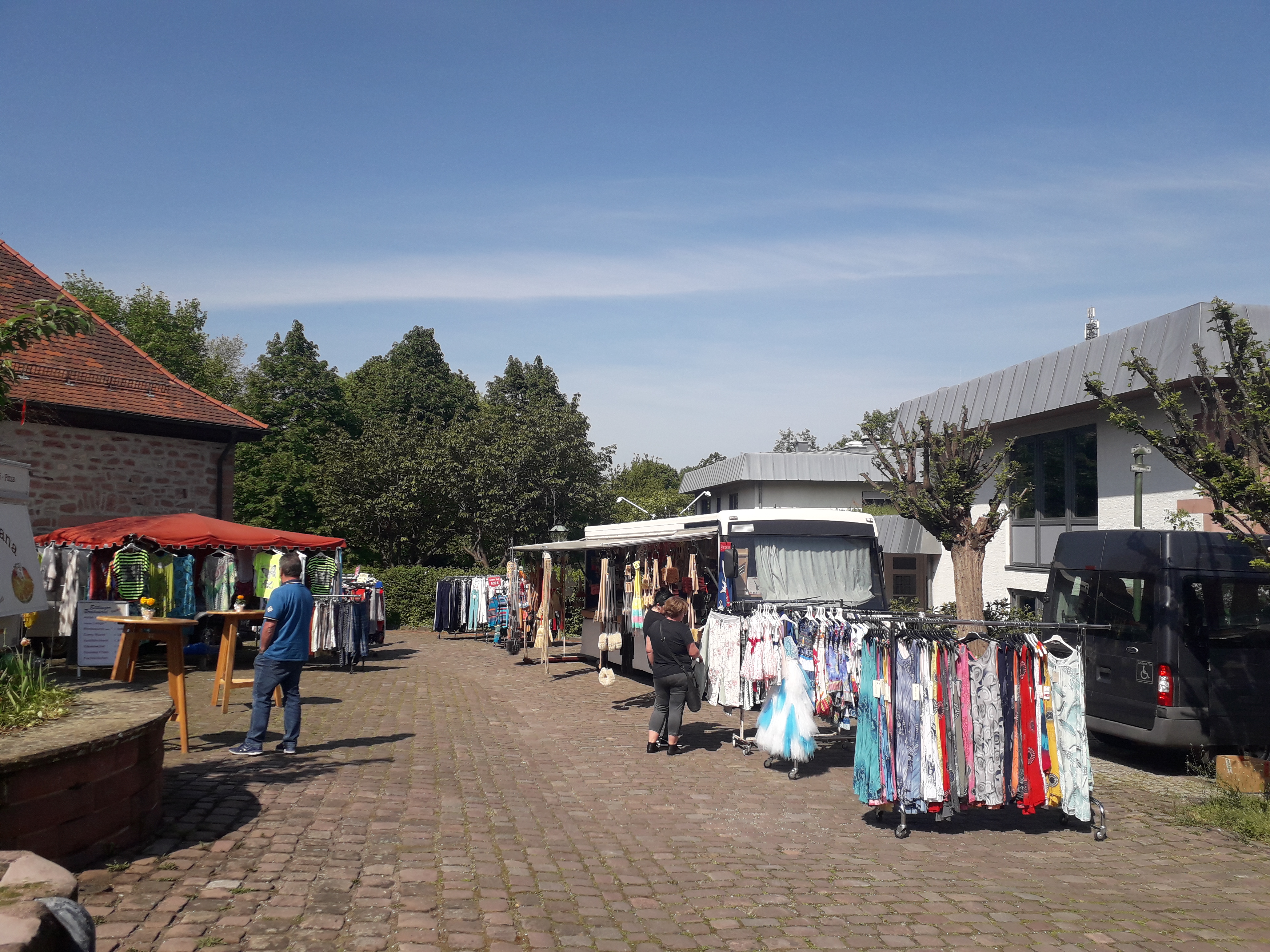 Auf diesem Bild sind zwei Maimarktstände vor der Kelter um die Gemeindehalle, mit Kleidung zu Verkauf, zu sehen.